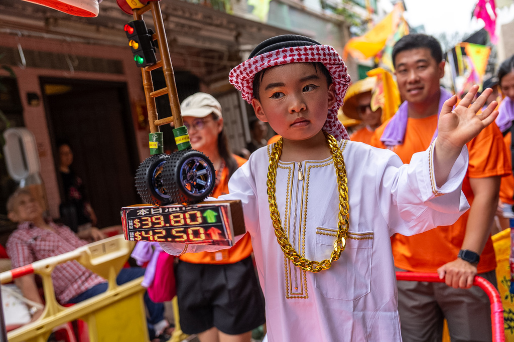 A child participates in the Piu Sik Parade with a replica gas station price sign model at the Bun Festival in Cheung Chau Island in Hong Kong, Sunday, May 24, 2026. (AP Photo/Chan Long Hei)