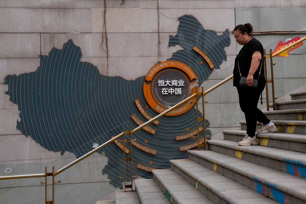 ARCHIVO - Una mujer camina junto a un mapa que muestra proyectos inmobiliarios de Evergrande en China, mientras se dirige a la plaza urbana Evergrande en Beijing el 18 de septiembre de 2023. (AP Foto/Andy Wong, Archivo)