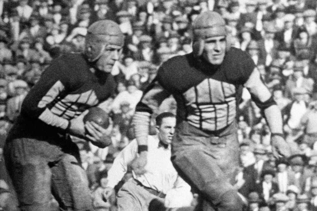 FILE - Illinois' Red Grange, left, follows a blocker on a 95-yard kickoff return for a touchdown against Michigan during a college football game on Oc.t 18, 1924, in Champaign, Ill. (AP Photo/File)