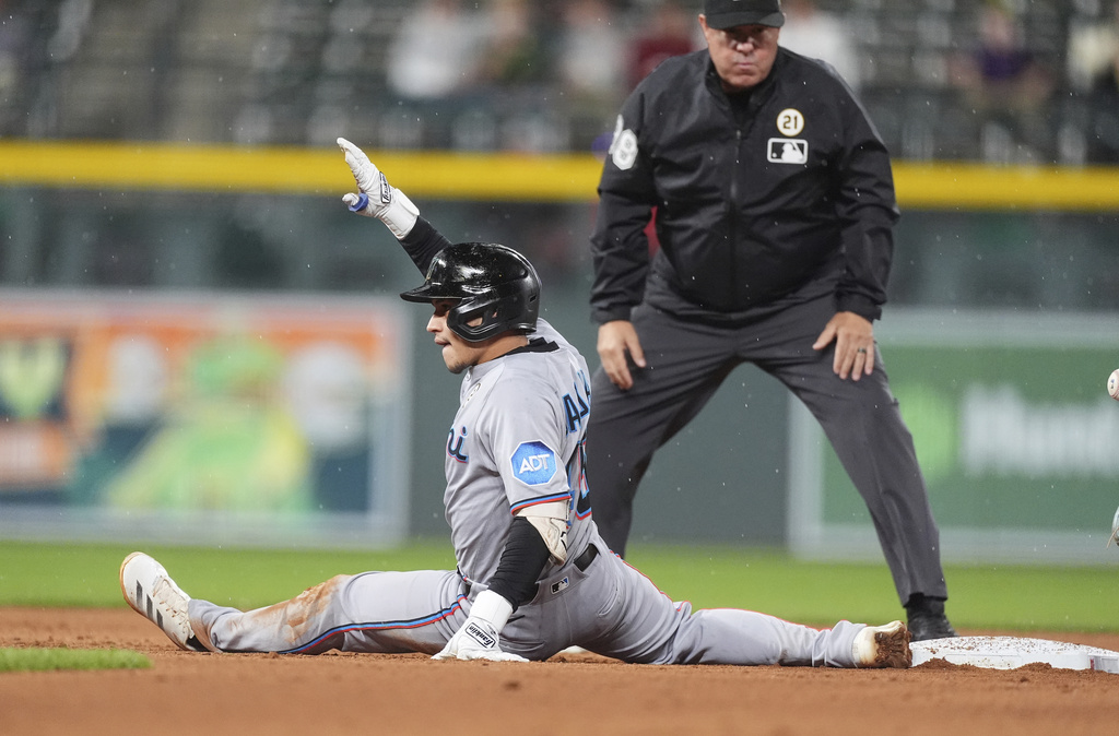 Miami Marlins' Javier Sanoja gestures to the dugout after reaching seocnd bse on an RBI double off Colorado Rockies starting pitcher Kyle Freeland as second base umpire Doug Eddings looks on in the sixth inning of a baseball game Tuesday, Sept. 16, 2025, in Denver. (AP Photo/David Zalubowski)