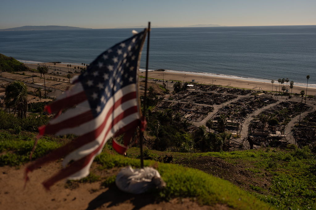 A tattered U.S. flag flaps in the wind over the remains of a mobile home park that was destroyed in the Palisades Fire along the Pacific Ocean, Friday, Dec. 5, 2025, in the Pacific Palisades neighborhood of Los Angeles. (AP Photo/Jae C. Hong)