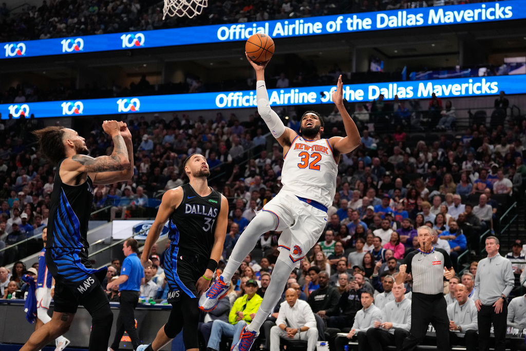New York Knicks center Karl-Anthony Towns (32) shoots against Dallas Mavericks defenders Klay Thompson (31) and Dereck Lively II in the first half of an NBA basketball game Wednesday, Nov. 19, 2025, in Dallas. (AP Photo/Tony Gutierrez)