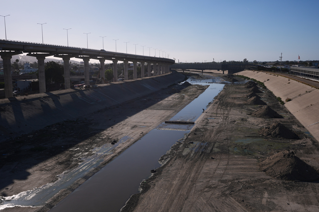 A man walks along the an aqueduct holding the Tijuana River as it arrives to the border and enters the United States, above, from Tijuana, Mexico, Wednesday, April 8, 2026. (AP Photo/Gregory Bull)