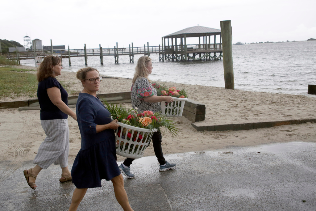 People bring baskets of flowers to place in front of the American Fish Company following a fatal shooting that occurred here the night before, Sunday, Sept. 28, 2025, in Southport, N.C. (AP Photo/Chris Seward)