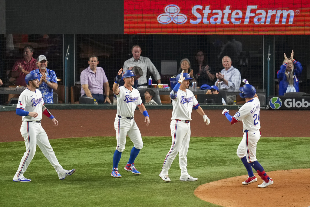 Texas Rangers' Michael Helman, right, is greeted near home plate by teammates, from left, Jonah Heim, Dylan Moore and Kyle Higashioka after scoring them all on a grand slam off Milwaukee Brewers starting pitcher Jose Quintana during the fifth inning of a baseball game Monday, Sept. 8, 2025, in Arlington, Texas. (AP Photo/Julio Cortez)