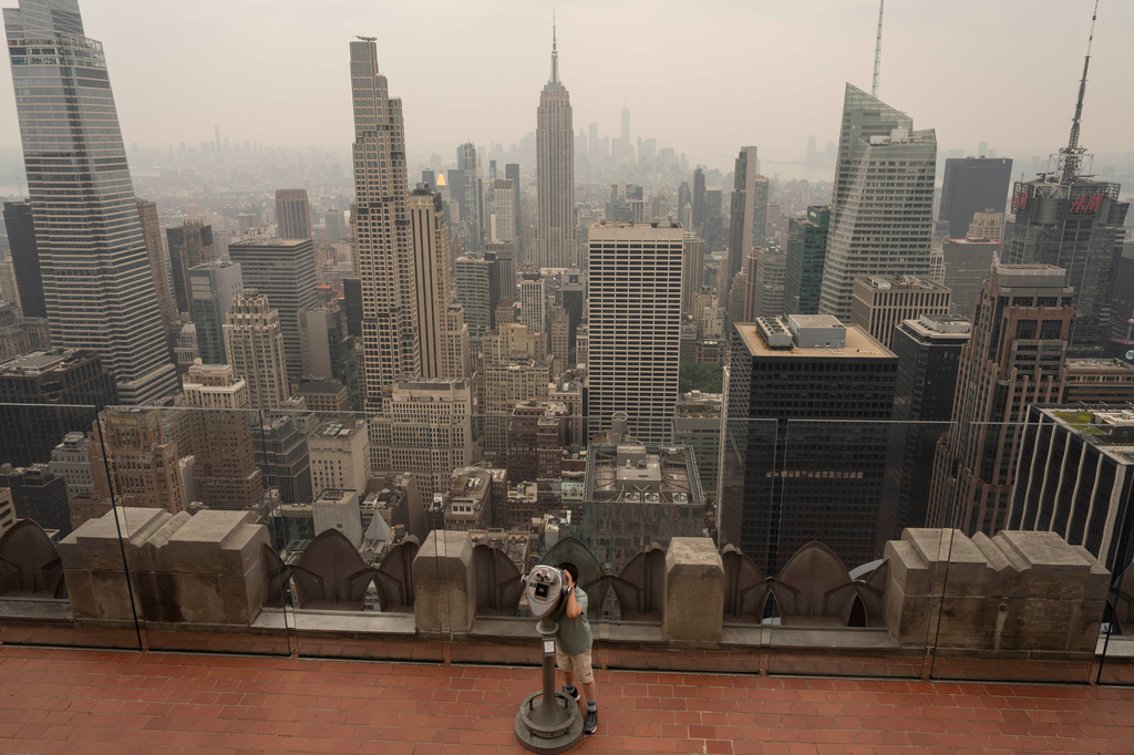 A person uses binoculars to look out as smoke from wildfires blankets the sky at Top of The Rock observation deck at the Rockefeller Center, Thursday, July 16, 2026, in New York. (AP Photo/Yuki Iwamura)