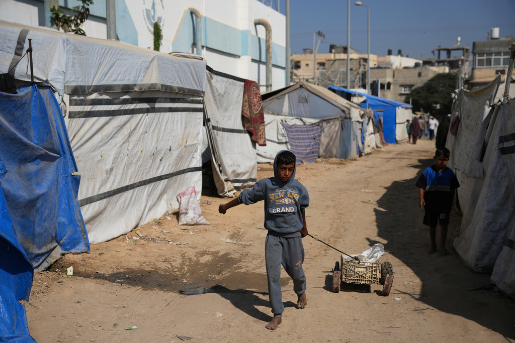 A Palestinian child pulls a cart between tents temporarily erected in a camp in Deir al‑Balah, central Gaza Strip, Saturday, Nov. 1, 2025. (AP Photo/Abdel Kareem Hana)