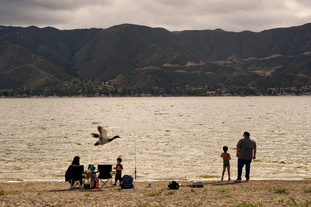 Visitors stand and sit along the shore at Wiskers Fishing Beach in Lake Elsinore, Calif., on Tuesday, April 21, 2026. (AP Photo/Damian Dovarganes)