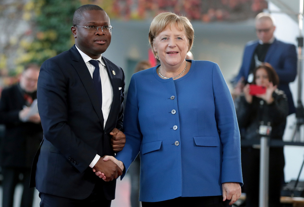 FILE - Benin's Economy and Finance Minister Romuald Wadagni, left, and German Chancellor Angela Merkel shake hands prior to a meeting at the chancellery as part of the "Compact with Africa" conference, in Berlin, Nov. 19, 2019. (AP Photo/Michael Sohn, File)