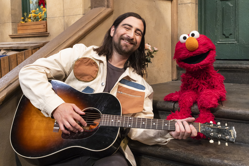 This image released by Sesame Workshop shows singer Noah Kahan, left, with muppet character Elmo on the set of "Sesame Street." (Zach Hyman/Sesame Workshop via AP)