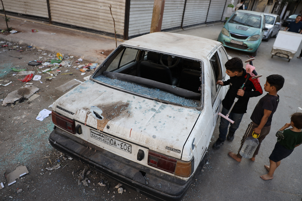 Children look at a damaged car in the Saif al-Dawla district of Aleppo, Syria, Tuesday, Oct. 7, 2025, following overnight clashes between Syrian government troops and the Kurdish-led Syrian Democratic Forces. (AP Photo/Omar Albam)