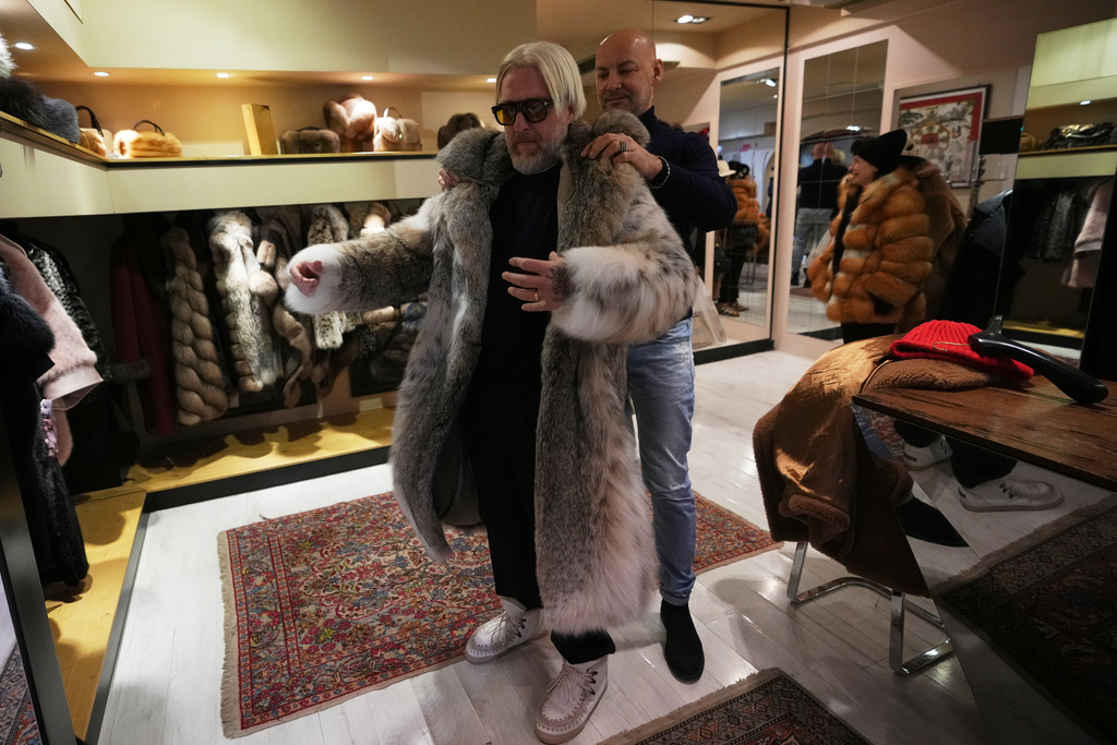 Sales manager for Pajaro, a luxury Italian fashion brand, Marco Molinari, right, helps his client, Stefano Vannicola, put on a fur coat in Cortina d'Ampezzo, Italy, Saturday, Feb. 14, 2026. (AP Photo/Alessandra Tarantino)