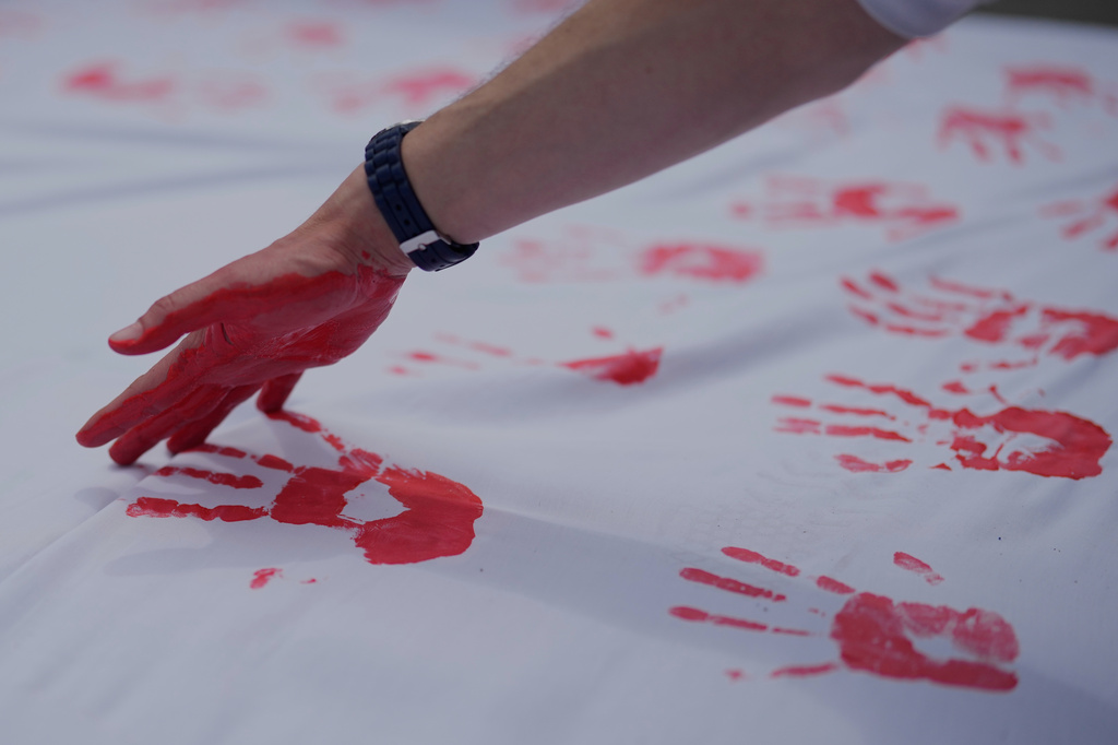 FILE - People cover a sheet in handprints at an event marking Red Hand Day, also known as the International Day against the Use of Child Soldiers, in Bogota, Colombia, where illegal armed groups recruit children, Feb. 12, 2026. (AP Photo/Fernando Vergara, File)