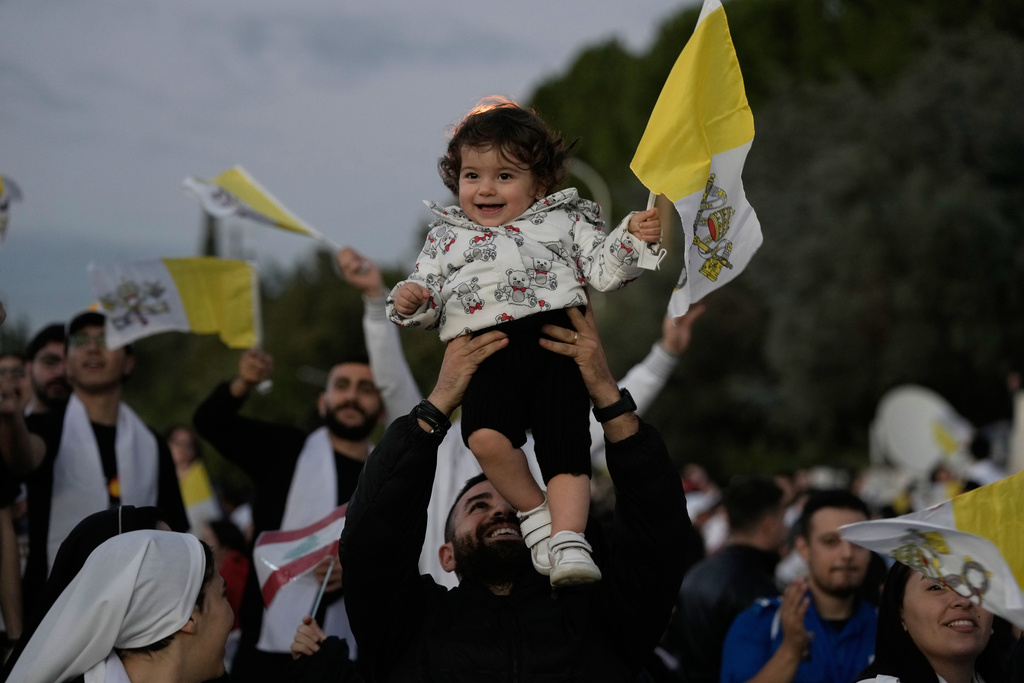 A man lifts a child holding a Vatican flag ahead of a visit by Pope Leo XIV to Bkerki, the seat of the Maronite Church, in Lebanon, Monday, Dec. 1, 2025. (AP Photo/Bilal Hussein)