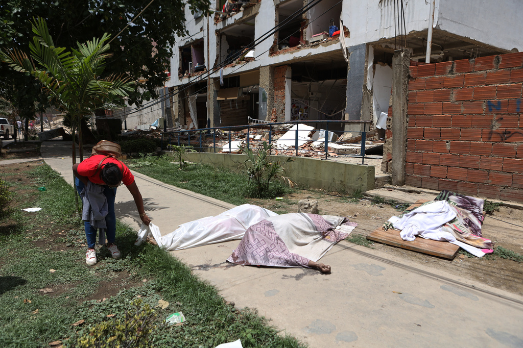 A man looks at covered bodies in front of a damaged building the day after earthquakes and several aftershocks struck La Guaira, Venezuela, Thursday, June 25, 2026. (AP Photo/Pedro Mattey)