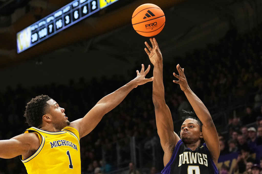 Washington guard Quimari Peterson, right, shoots against Michigan guard Trey McKenney, left, during the first half of an NCAA college basketball game Wednesday, Jan. 14, 2026, in Seattle. (AP Photo/Lindsey Wasson)