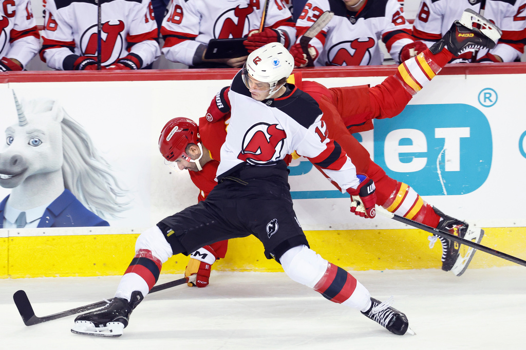 New Jersey Devils' Cody Glass (12) collides with Calgary Flames' Nazem Kadri, back, during first-period NHL hockey game action in Calgary, Alberta, Monday, Jan. 19, 2026. (Larry MacDougal/The Canadian Press via AP)
