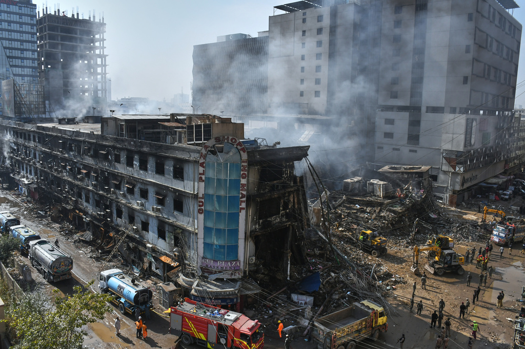Rescue workers and firefighters work with heavy machinery to clear the rubble of a burnt building of a multi-story shopping plaza following a massive fire in Karachi, Pakistan, Tuesday, Jan. 20, 2026. (AP Photo/Ali Raza)