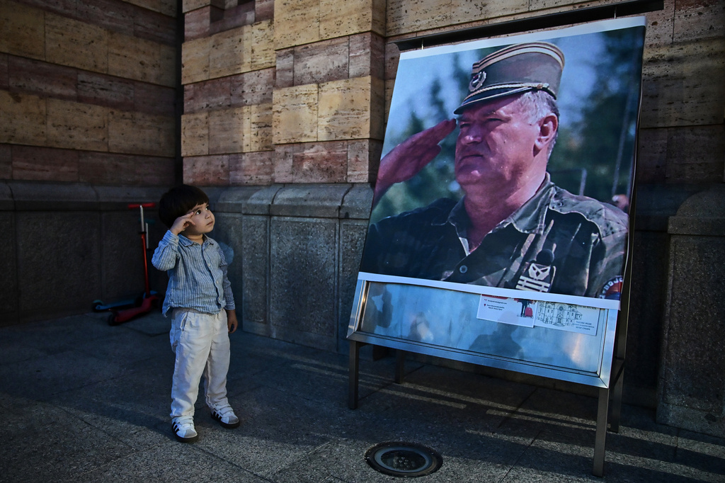 A boy salutes in front of poster of former Bosnian Serb wartime general Ratko Mladic, outside a church in Banja Luka, Bosnia-Herzegovina, Thursday, Aug. 27, 2026. (AP Photo/Radivoje Pavicic)