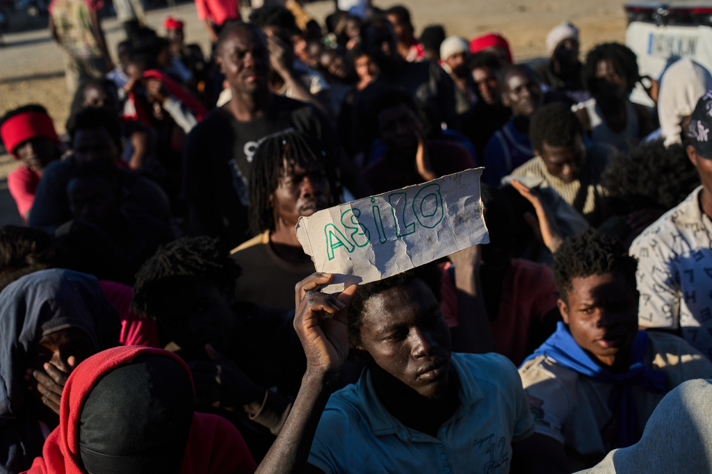 A migrant who crossed from Morocco into Spain holds a sign reading, in Spanish, "asylum" as he lines up for food distribution on a beach in the Spanish enclave of Ceuta, Monday, Aug. 3, 2026. (AP Photo/Bernat Armangue)