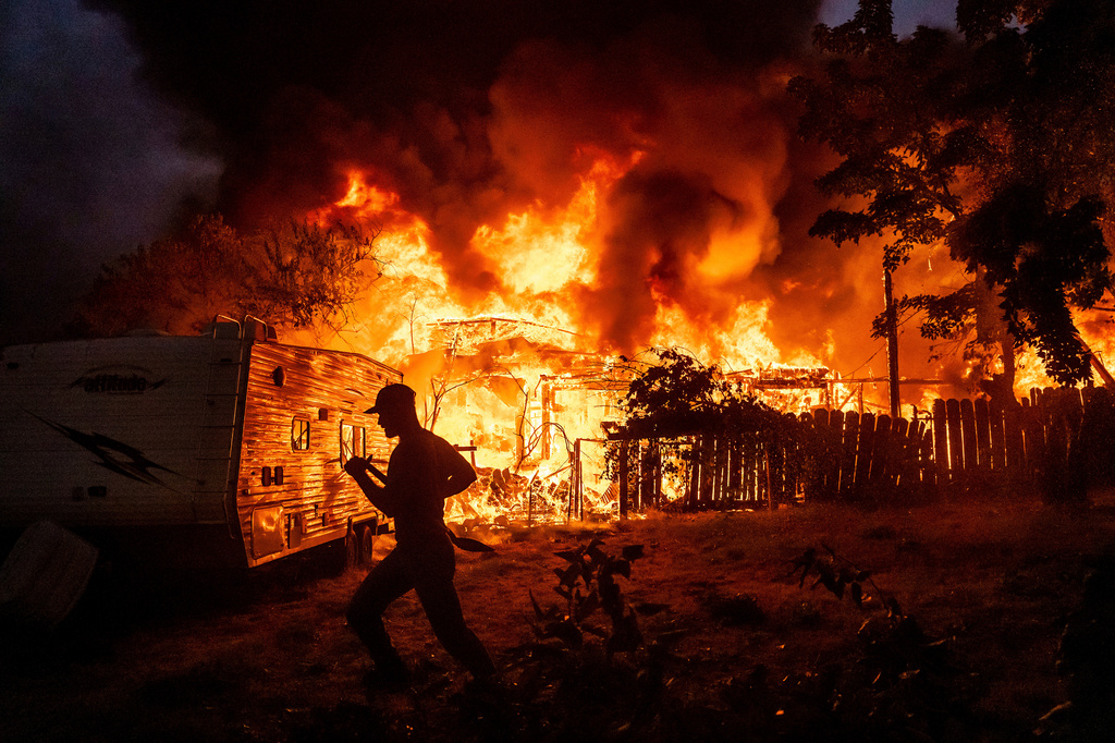 FILE - A residents works to stop flames from a burning home from spreading to a neighboring house as the 6-5 Fire burns through the Chinese Camp community of Tuolumne County, Calif., Sept. 2, 2025. (AP Photo/Noah Berger, File)