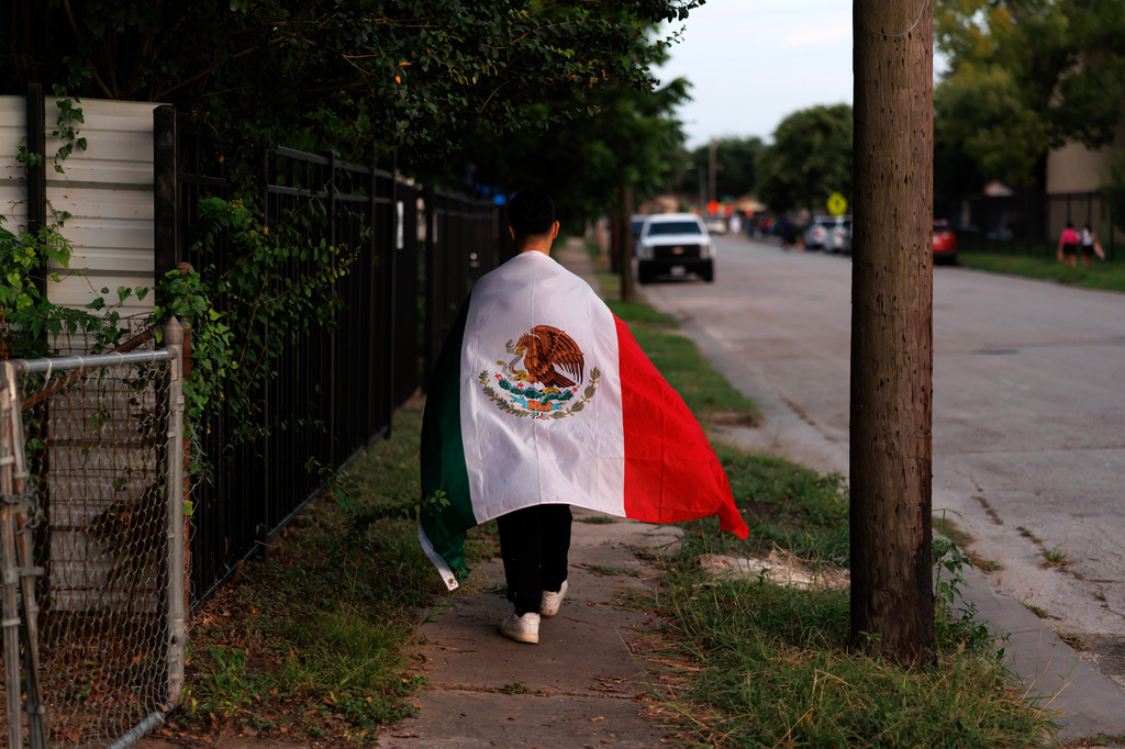 A man walks home draped in a Mexican flag after a vigil for Lorenzo Salgado Araujo, a Mexican national fatally shot by a federal immigration agent a day prior, Wednesday, July 8, 2026, in Houston. (AP Photo/Mark Felix)