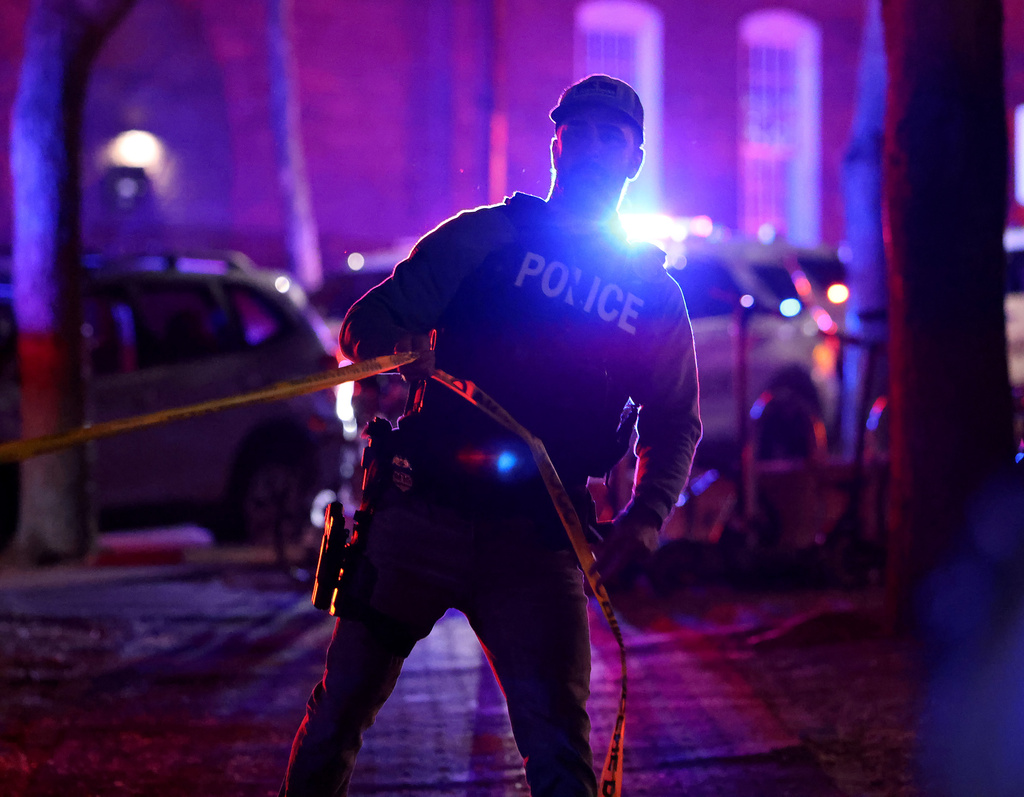 A police officer hangs yellow crime tape at Brown University in Providence, R.I., on Saturday, Dec. 13, 2025, during the investigation of a shooting. (AP Photo/Mark Stockwell)