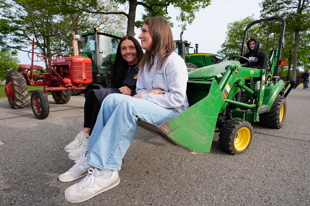 Liv Tilley, left, Chloie Lemke, right, ride in a front loader driven by Jonathan Tarczynski during Tractor Day for graduating seniors at Airport High School Friday, May 22, 2026, in Carleton, Mich. (AP Photo/Paul Sancya)
