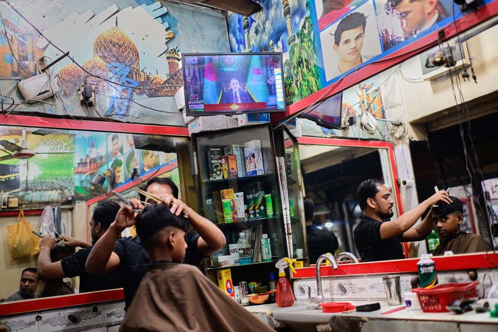 A man gets a haircut in a salon where a television broadcasts Bangladesh's Chief Election Commissioner A.M.M. Nasir Uddin's address to the nation, in Dhaka, Bangladesh, Thursday, Dec. 11, 2025. (AP Photo/Mahmud Hossain Opu)