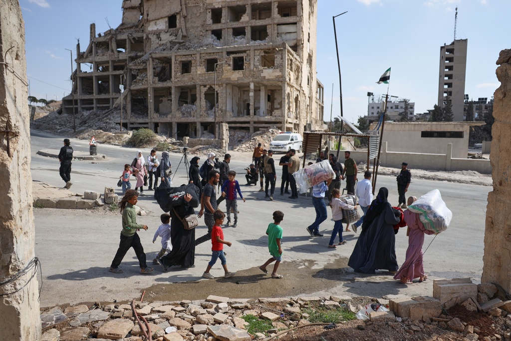 Residents walk past a security forces checkpoint as they leave the Sheikh Maqsoud and Achrafieh neighborhoods of Aleppo, Syria, Tuesday, Oct. 7, 2025, following overnight clashes between Syrian government troops and the Kurdish-led Syrian Democratic Forces. (AP Photo/Omar Albam)