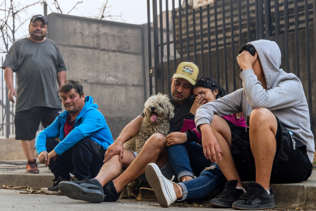 Members of the Gonzalez family sit on a sidewalk after their home caught fire during wildfires near Lirquen, Chile, Sunday, Jan. 18, 2026. (AP Photo/Javier Torres)