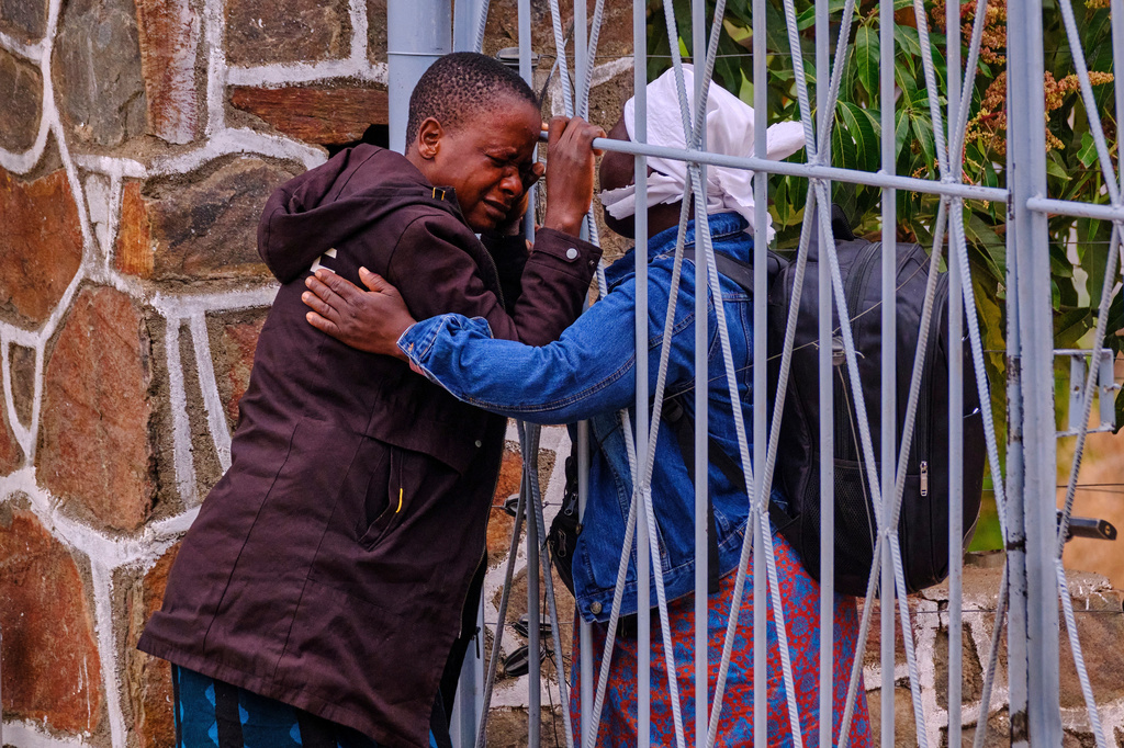 Philis Hamandise, center, is embraced through a gate by a colleague at a victim identification center after losing her 9-year-old daughter and 6-year-old nephew in a ferry capsizing on Lake Kariba, in Kariba, Zimbabwe, Thursday, Aug. 13, 2026. (AP Photo/Mkhululi Thobela)