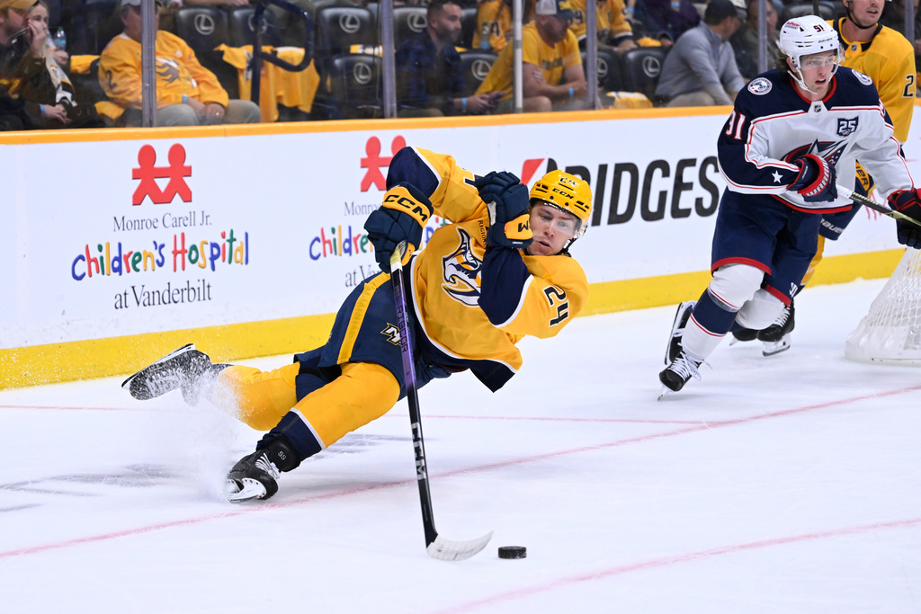 Nashville Predators defenseman Spencer Stastney (24) slips as he turns up the ice with Columbus Blue Jackets center Kent Johnson (91) following during the first period of an NHL hockey game Thursday, Oct. 9, 2025, in Nashville, Tenn. (AP Photo/John Amis)