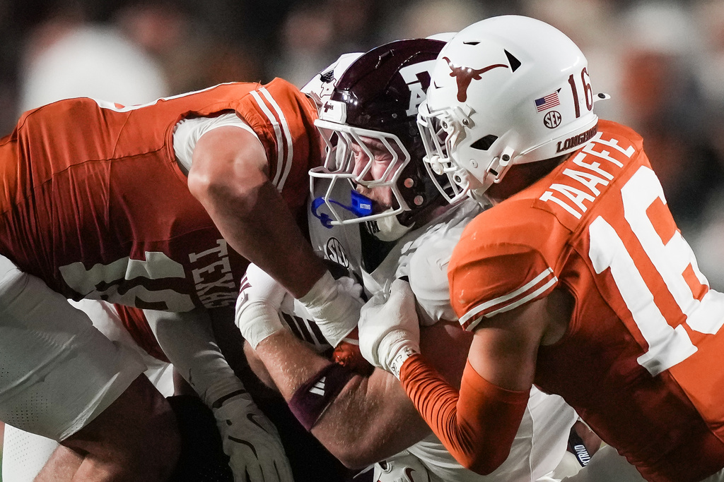 Texas defensive back Warren Roberson (24) and linebacker Liona Lefau (18) bring down Texas A&M tight end Theo Melin Öhrström (17) during the second quarter of an NCAA college football game against Texas A&M in Austin, Texas, Friday, Nov. 28, 2025. (Sara Diggins/Austin American-Statesman via AP)