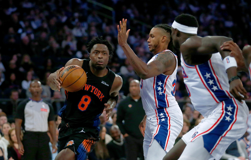 New York Knicks forward OG Anunoby, left, dribbles around Philadelphia 76ers forward Jabari Walker, middle, and center Adam Bona, right, during the first half of an NBA basketball game, Friday, Dec. 19, 2025, in New York. (AP Photo/John Munson)