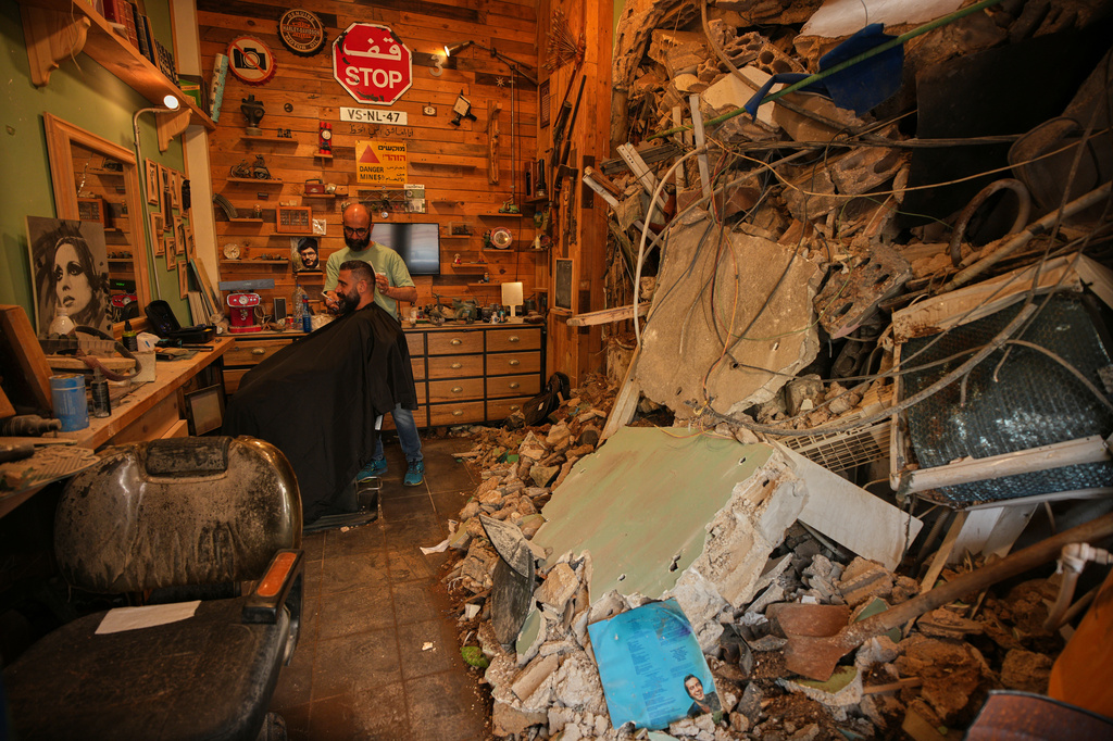 Barber Mohammad Mehdi cuts the hair of his client Ayman Al Zein inside his shop, which was damaged in an Israeli airstrike that also damaged Al Zein's shop, in Dahiyeh, Beirut's southern suburbs, Lebanon, Saturday, April 18, 2026. (AP Photo/Hassan Ammar)