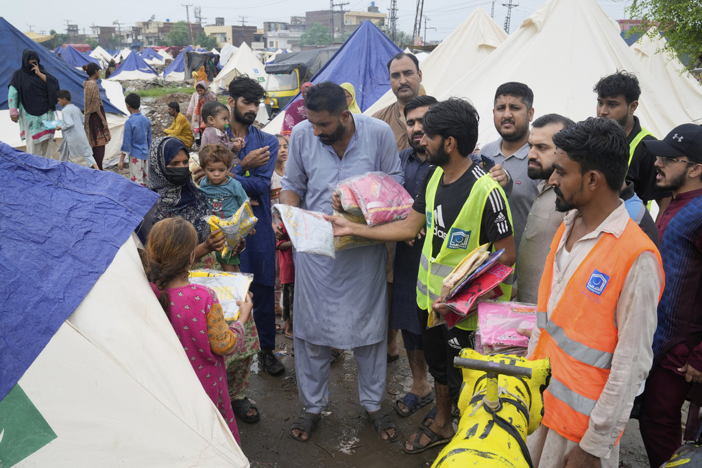 Volunteers distribute clothes among families at a relief camp set up for people who fled their homes following torrential rains and rising water level in the Ravi river, on the outskirts of in Lahore, Pakistan, Sunday, Aug. 31, 2025. (AP Photo/K.M. Chaudary)
