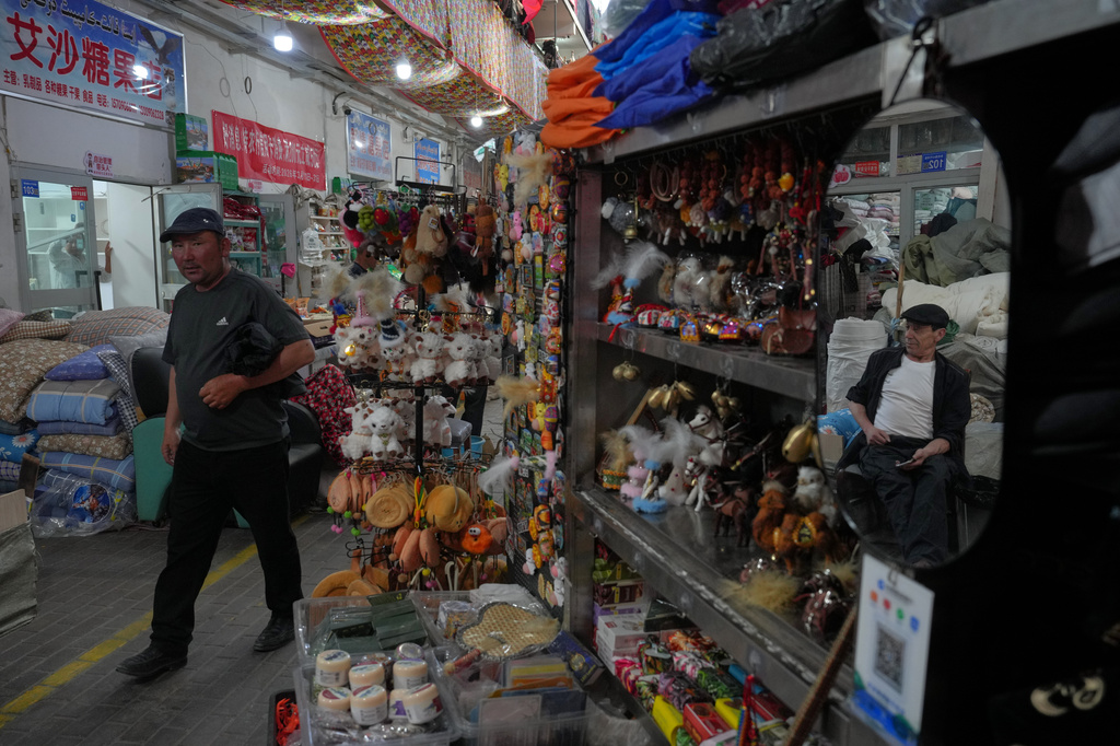A man walks by a vendor reflecting on a mirror as he waits for customers at his store inside the Jinshan market in Altay Prefecture, northwest China's Xinjiang Uyghur Autonomous Region, Wednesday, June 10, 2026. (AP Photo/Andy Wong)