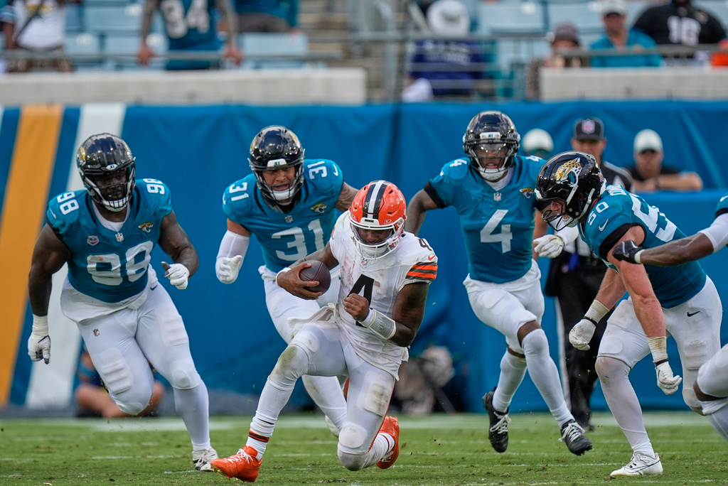 Cleveland Browns quarterback Deshaun Watson (4) runs from Jacksonville Jaguars Albert Regis (98), Jahlani Tavai (31), cornerback Jarrian Jones (4) and Branson Combs (5) in the second half of an NFL football game, Sunday, Sept. 13, 2026, in Jacksonville. (AP Photo/Mike Stewart)