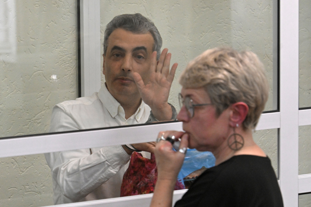 Lev Shlosberg, left, senior member of the Yabloko party, waves standing in the defendant's box after a verdict in the case against him is delivered, in a court in Pskov, Russia, Monday, Aug. 17, 2026, with his wife Zhanna Shlosberg on the right. (AP Photo)