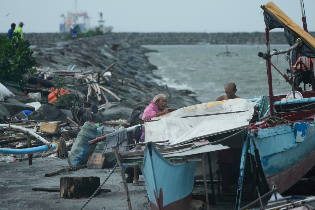 A woman and man secure their shelter as rain pours due to Typhoon Fung-wong on Monday, Nov. 10, 2025, in Manila, Philippines. (AP Photo/Aaron Favila)