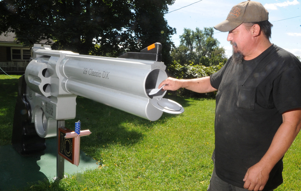 FILE - In this photo taken Thursday, Sept. 5, 2013, Roger Buchko grabs mail from his mailbox that resembles a giant Smith & Wesson .44 magnum revolver in Lopatcong Township, N,J. Mail is placed in a small compartment at the mouth of the gigantic gun barrel. (AP Photo/The Express-Times, Sue Beyer, File)