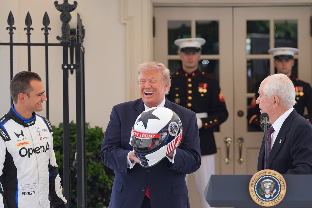 President Donald Trump reacts after receiving a helmet as Alex Palou, the reigning IndyCar champion, left, and Roger Penske, chairperson and founder of Penske Corp., right, watch on West Executive Drive at the White House during a showcase for the upcoming Freedom 250 Grand Prix auto race, Monday, July 13, 2026, in Washington. (AP Photo/Alex Brandon)