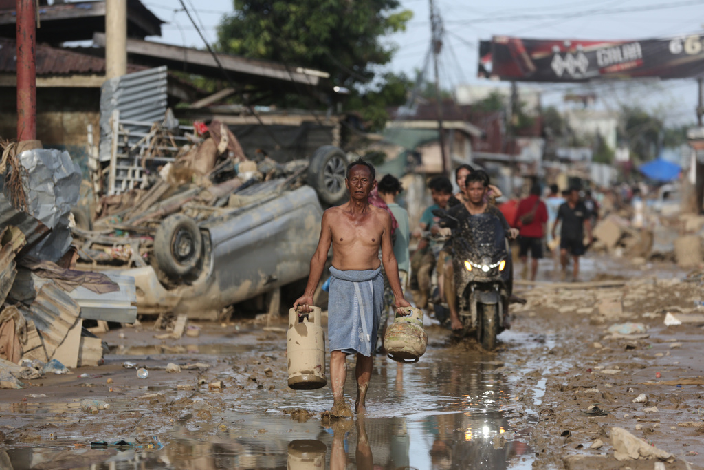 A survivor carries salvaged gas cylinders at an area affected by flash flood in Aceh Tamiang, on Sumatra Island, Indonesia, Thursday, Dec. 4, 2025. (AP Photo/Binsar Bakkara)