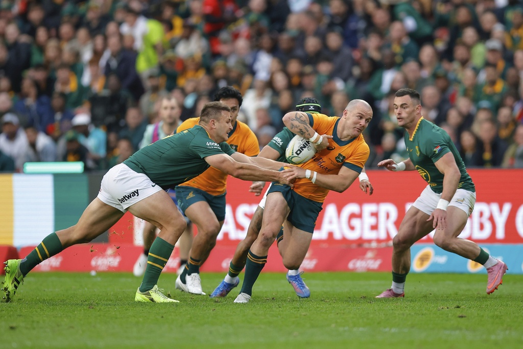 Australia's Dylan Pietsch, centre, being tackled by South Africa's Andre Esterhuizen, left, during a rugby championship test match between South Africa and Australia, at Ellis Park stadium in Johannesburg, South Africa, Saturday, Aug. 16, 2025. (AP Photo/Frans Lombard)