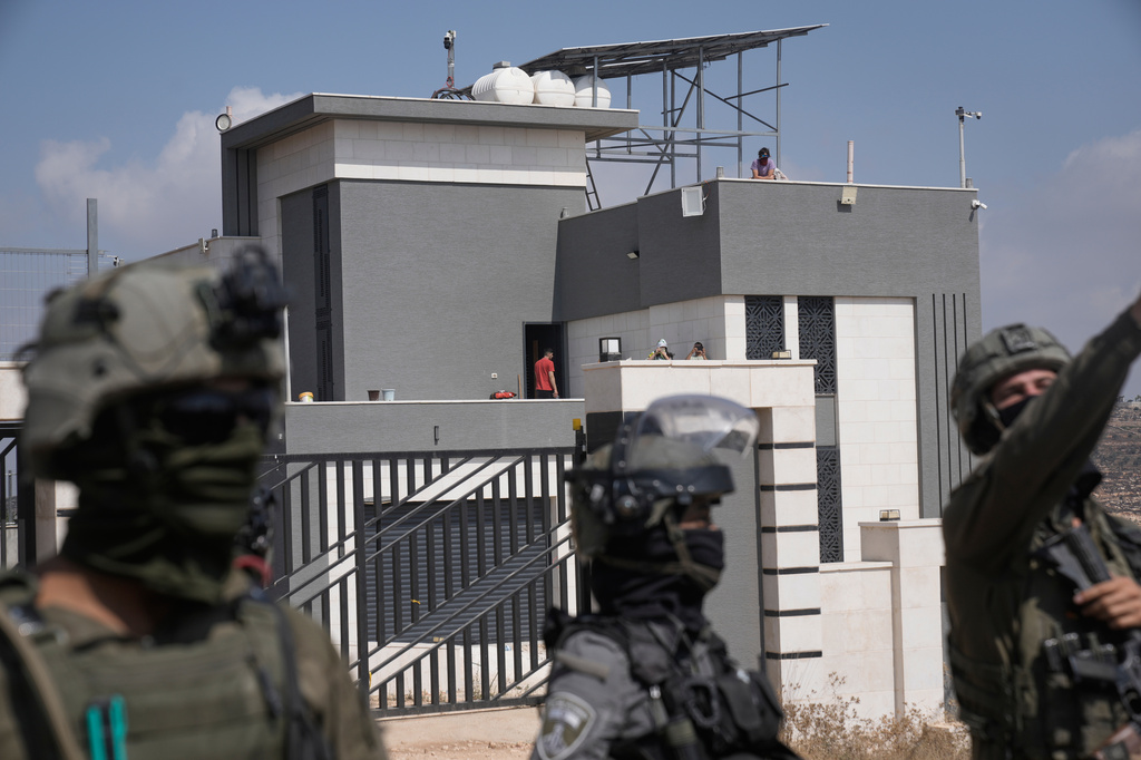Israeli army soldiers block the road leading to the houses of three Palestinian families that have been besieged by Israeli settlers for six days, while activists march to deliver food and water supplies for the residents, in the occupied West Bank village of Qusra, south of Nablus, Friday, Aug. 14, 2026. (AP Photo/Majdi Mohammed)