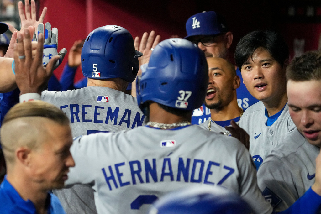 Los Angeles Dodgers' Freddie Freeman, left, and Teoscar Hernández, middle, are greeted by Mookie Betts, right center, and Shohei Ohtani, right, after the pair scored on Freeman's home run against the Arizona Diamondbacks during the fourth inning of a baseball game Thursday, Sept. 25, 2025, in Phoenix. (AP Photo/Darryl Webb)