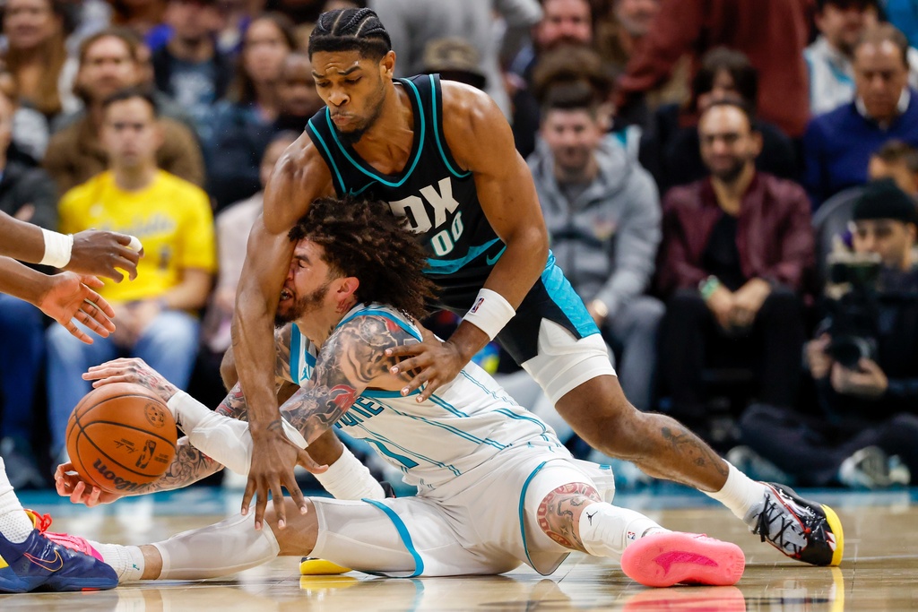 Charlotte Hornets guard LaMelo Ball, left, is fouled by Portland Trail Blazers guard Scoot Henderson (00) as they battle for a loose ball during the second half of an NBA basketball game in Charlotte, N.C., Saturday, Feb. 28, 2026. (AP Photo/Nell Redmond)