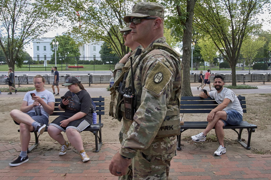 Armed members of the South Carolina National Guard patrol in Lafayette Parkl by the White House, as some people on benches react, Tuesday, Aug. 26, 2025, in downtown Washington. (AP Photo/Jacquelyn Martin)