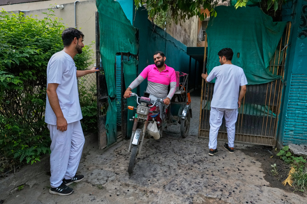Hamza Ali, 28, who lost both legs in a road accident, leaves for work, with his roommates helping him with the gate in Islamabad, Pakistan, Friday, July 17, 2026. (AP Photo/Anjum Naveed)